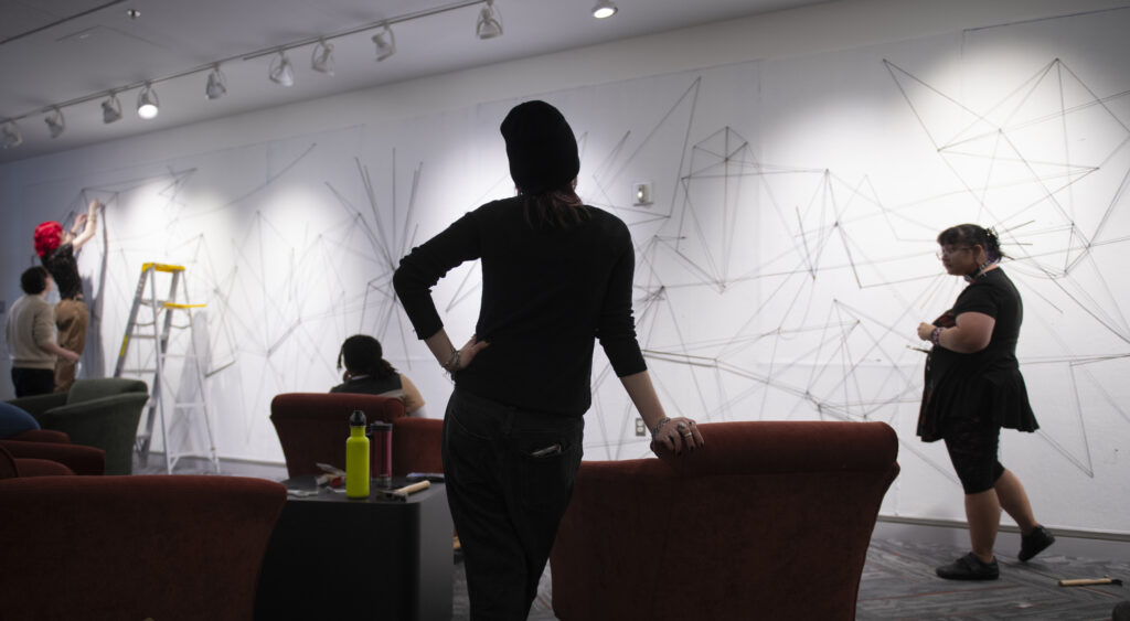 students assemble a mural of string and nail on wall