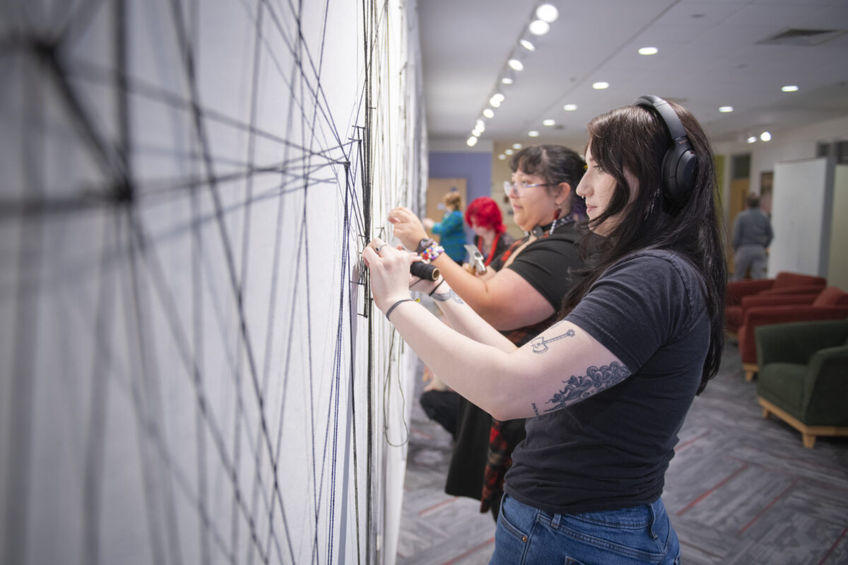 students assemble a mural of string and nail on wall