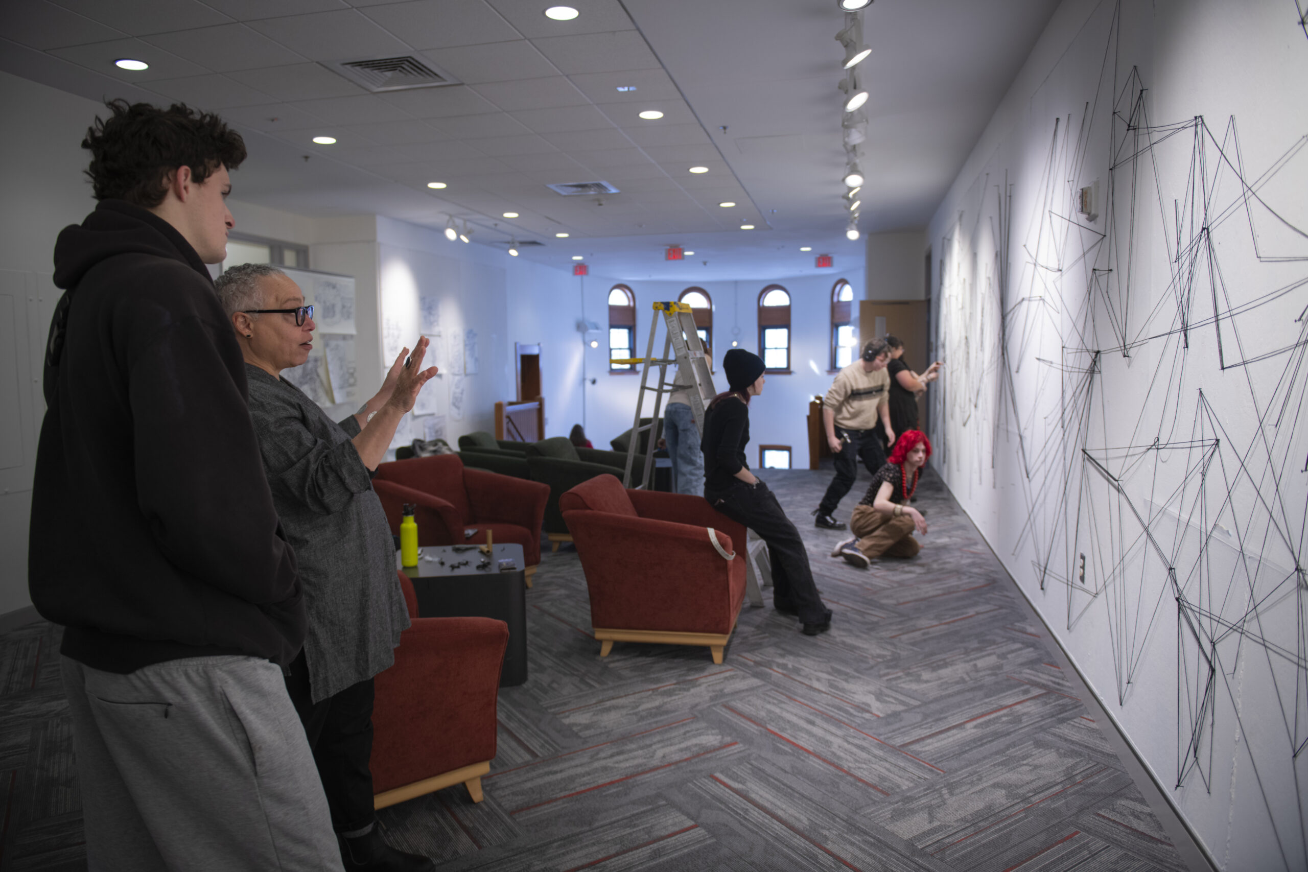 students assemble a mural of string and nail on wall