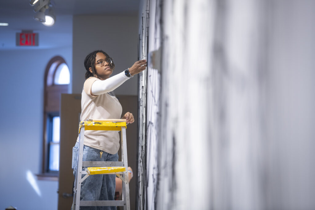 students assemble a mural of string and nail on wall