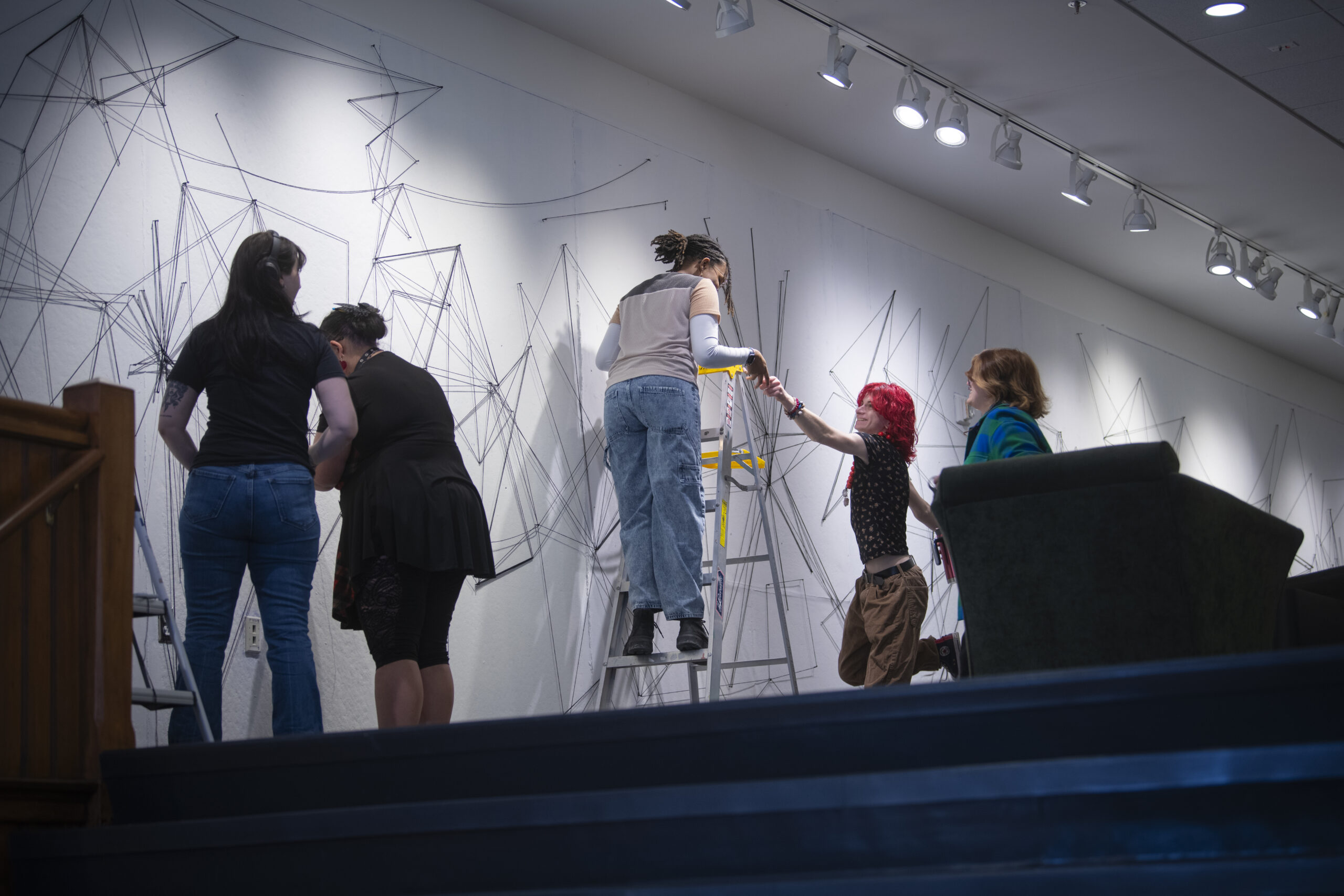 students assemble a mural of string and nail on wall