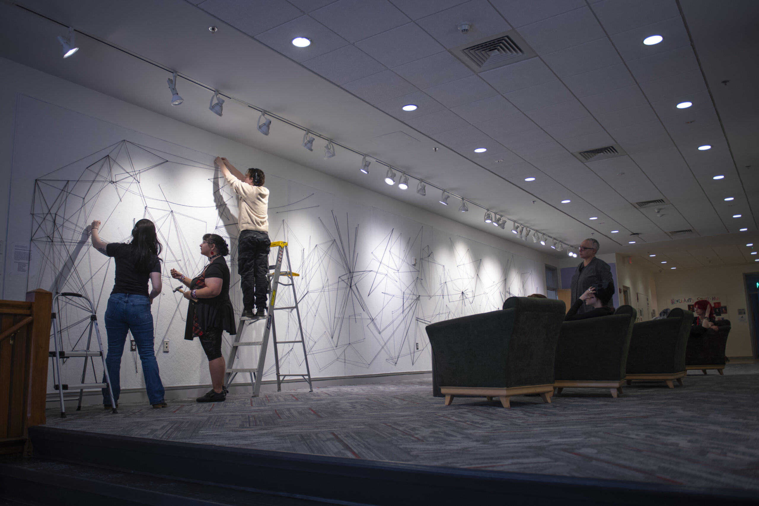 students assemble a mural of string and nail on wall