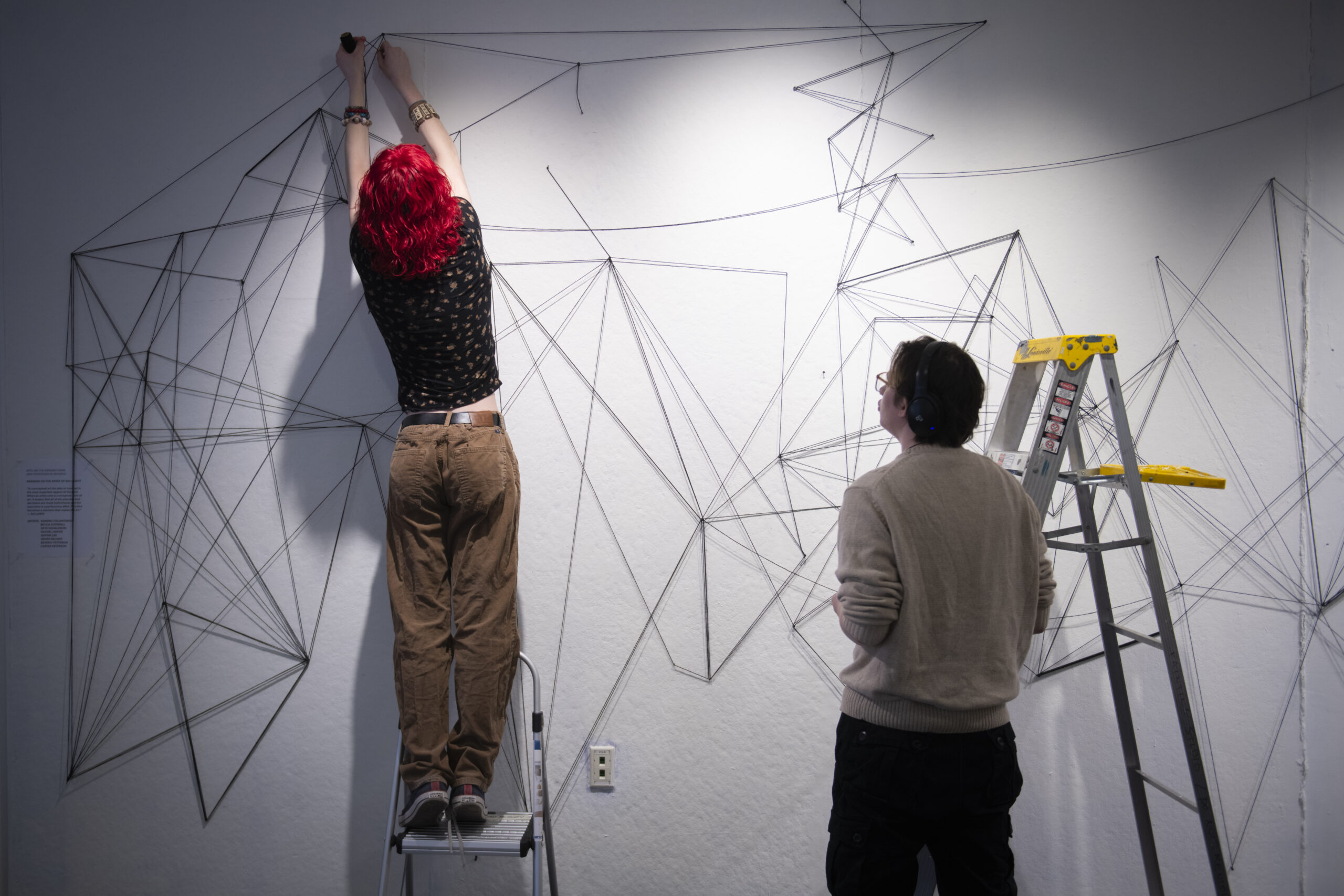 students assemble a mural of string and nail on wall