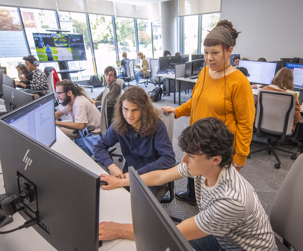 Professor Terrasa Ulm stands over students seated at computers in game design course
