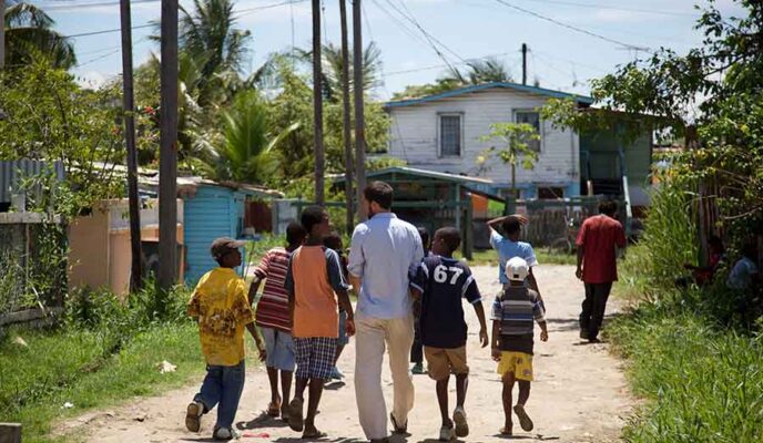 A Peace Corps volunteer walks down a road with young members of their host community