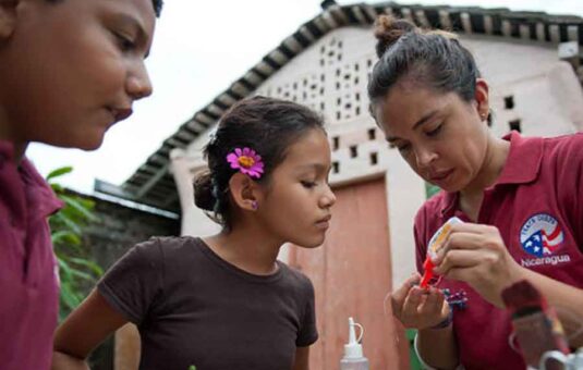 A Peace Corps volunteer working on a craft project with two children