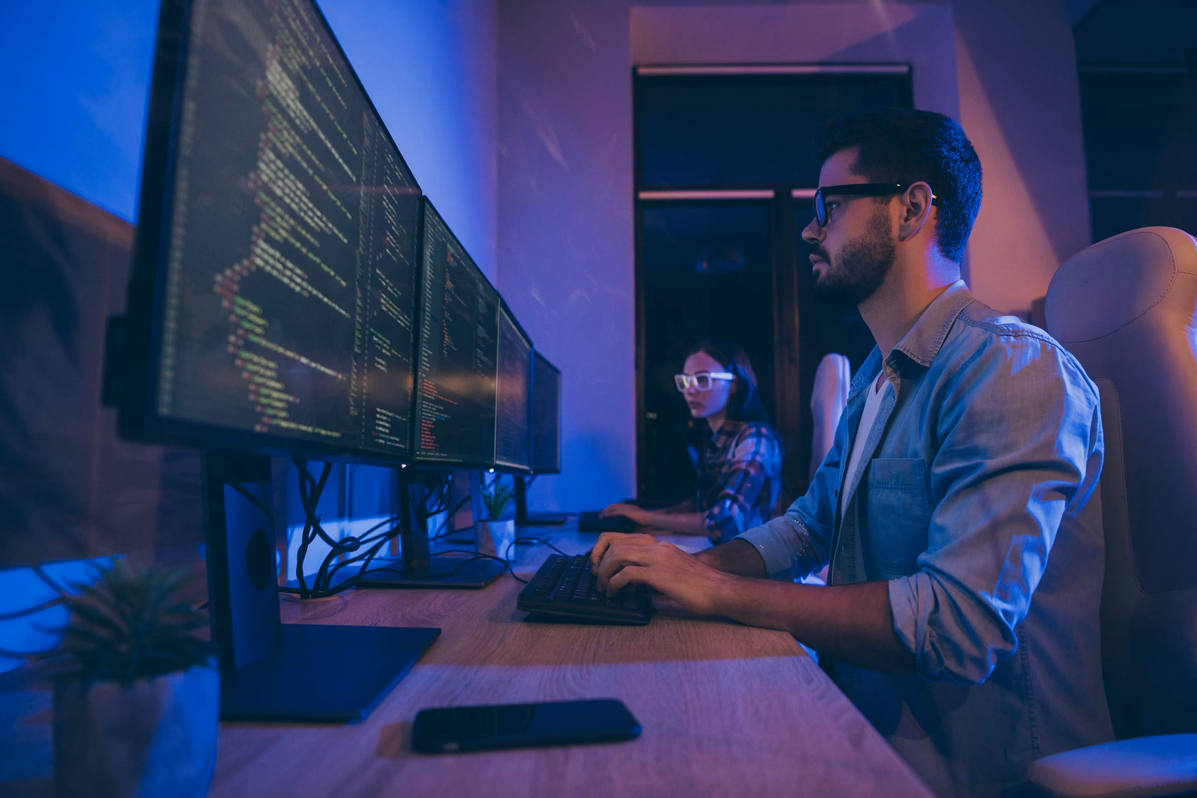 Two people seated before large monitors working on coding projects