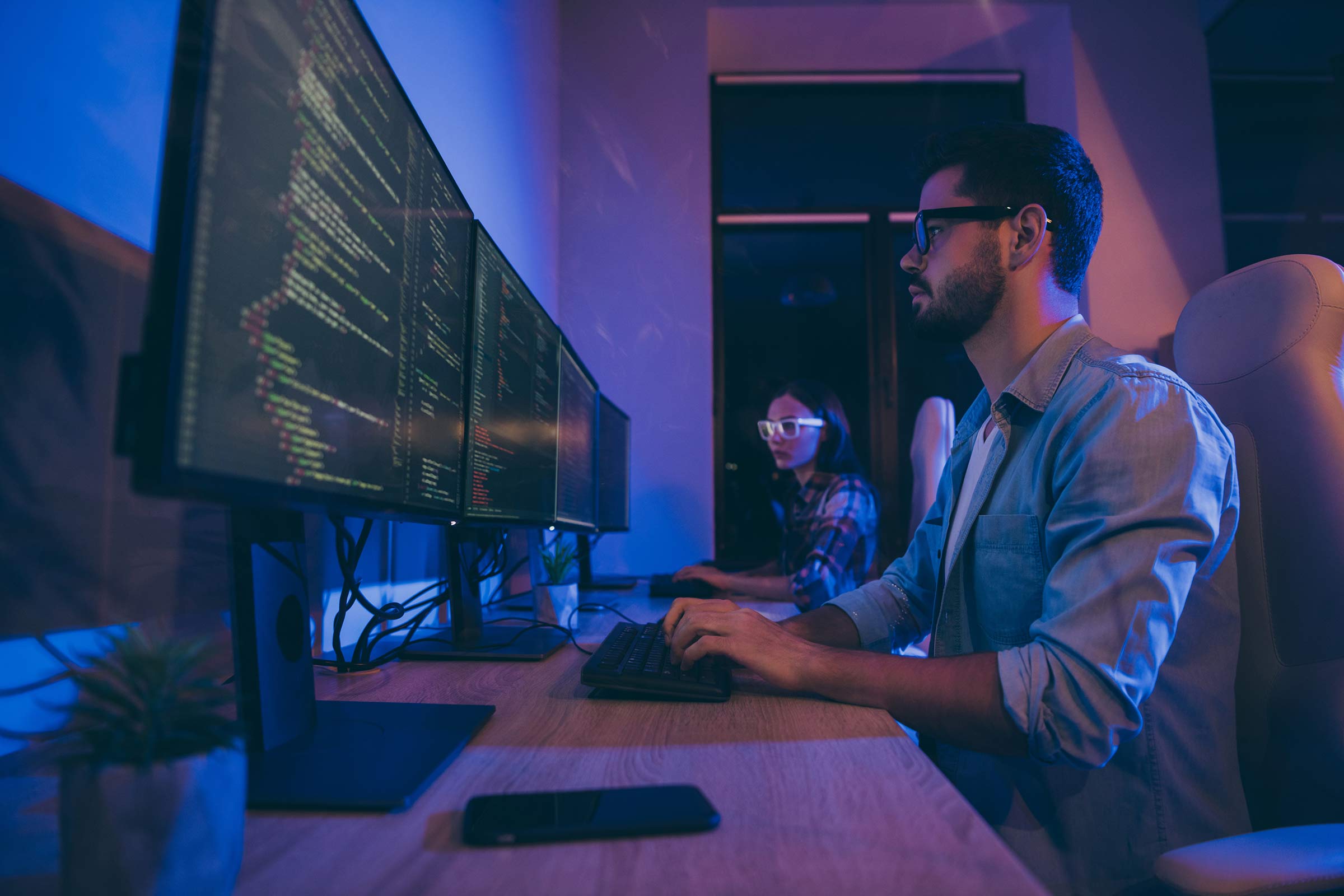 Two people seated before large monitors working on coding projects