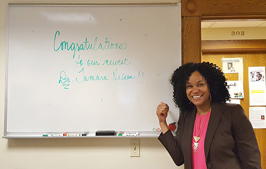 alumni member in front of white board with congratulations spelled out on it.