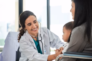 Public Health: Young female pediatric doctor teases little Asian boy before medical examination at outpatient clinic hospital, people public health care checkups, and appointment visits.