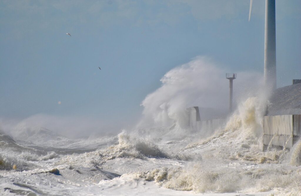 Rough surf battering a concrete wall below wind turbines