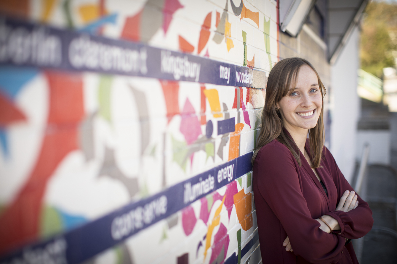 A student smiles, leaning against a mural in a community center