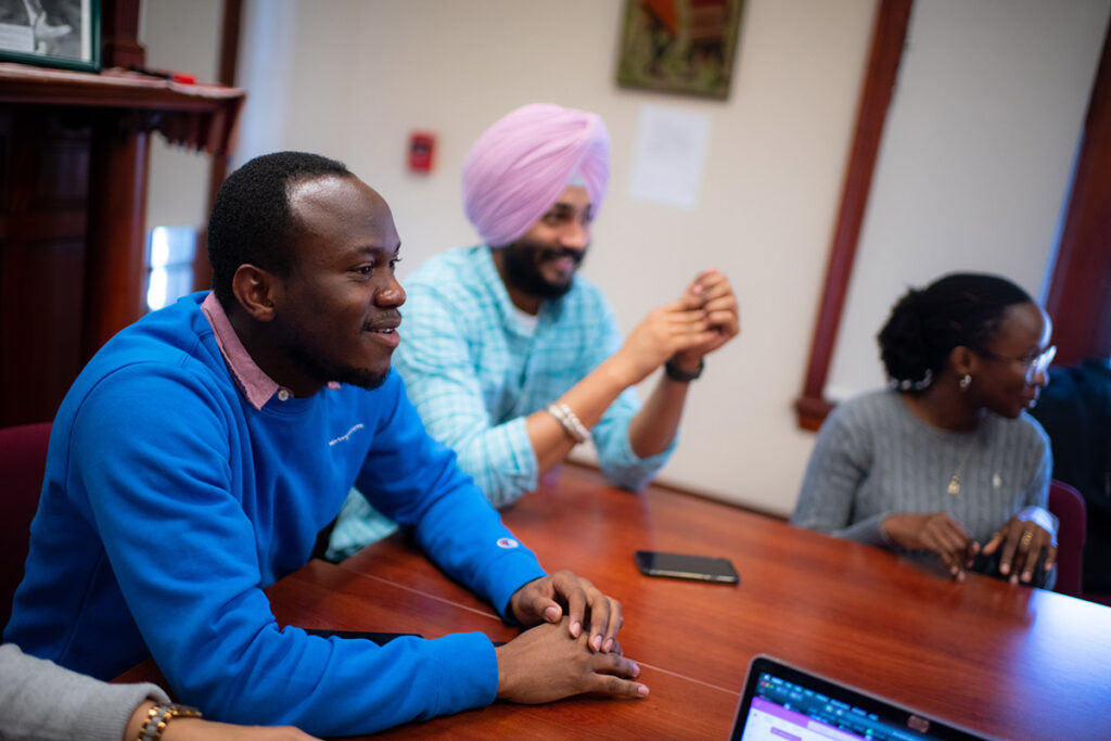 Students smiling, seated in a seminar classroom in the Department of Sustainability and Social Justice