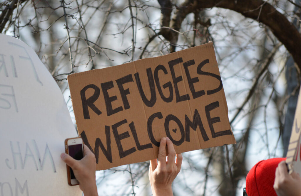 A person holding a homemade sign on cardboard that says 'refugees welcome'