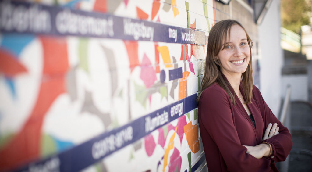 A student smiles, leaning against a mural in a community center