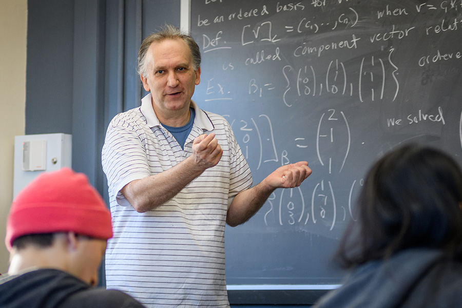 Math professor writing math code on chalk board in front of students