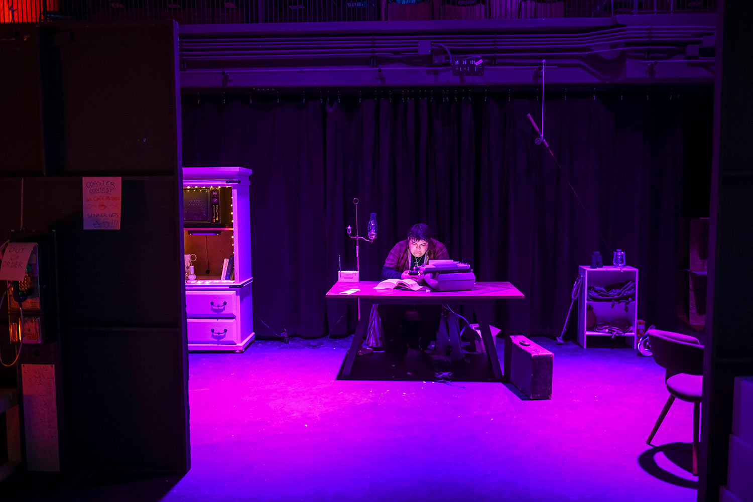 A student seated at a dimly illuminated table, dress rehearsal for Hacker’s Ostracon: An Interactive Performance