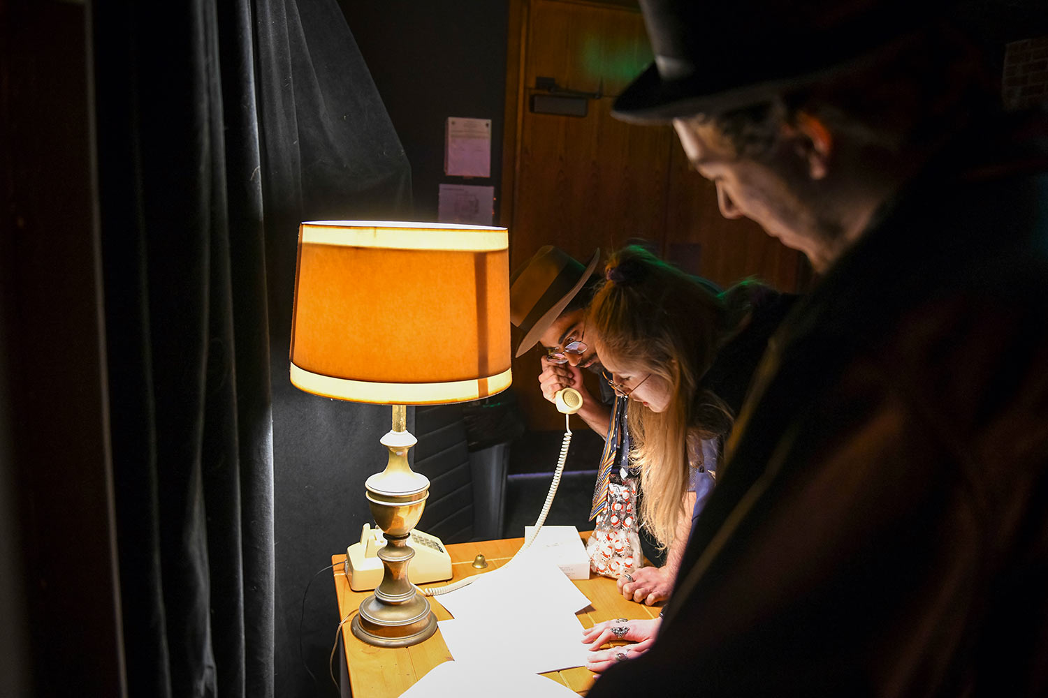 Students gather around a phone, dress rehearsal for Hacker’s Ostracon: An Interactive Performance