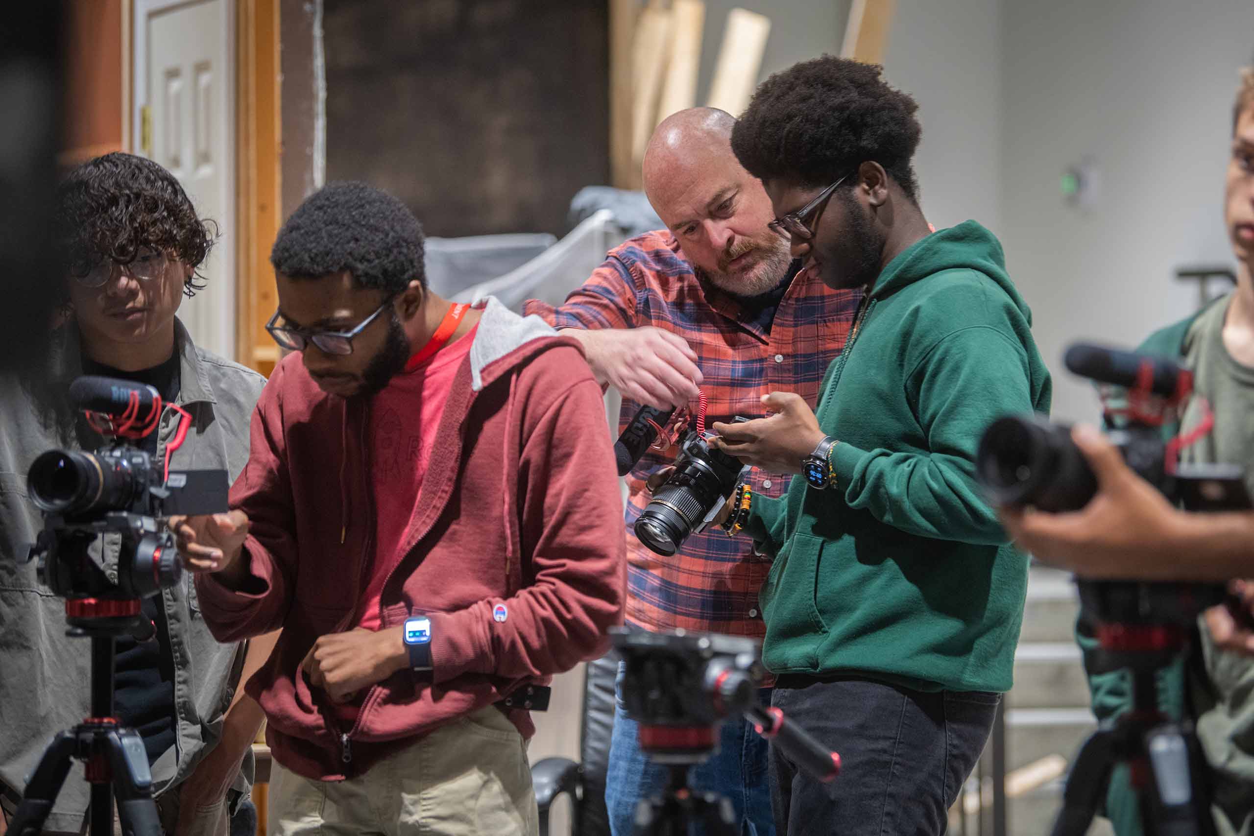 Students adjusting their camera settings during an Intro to Digital Filmmaking class while the professor assists