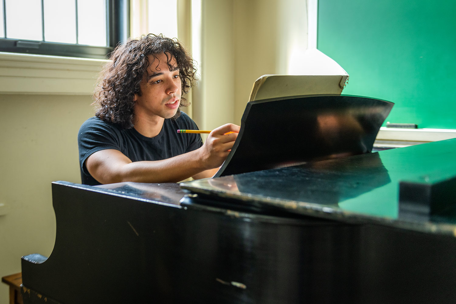 Robbie Wilson, making notes at a piano in a practice space, Estabrook Hall, Clark University