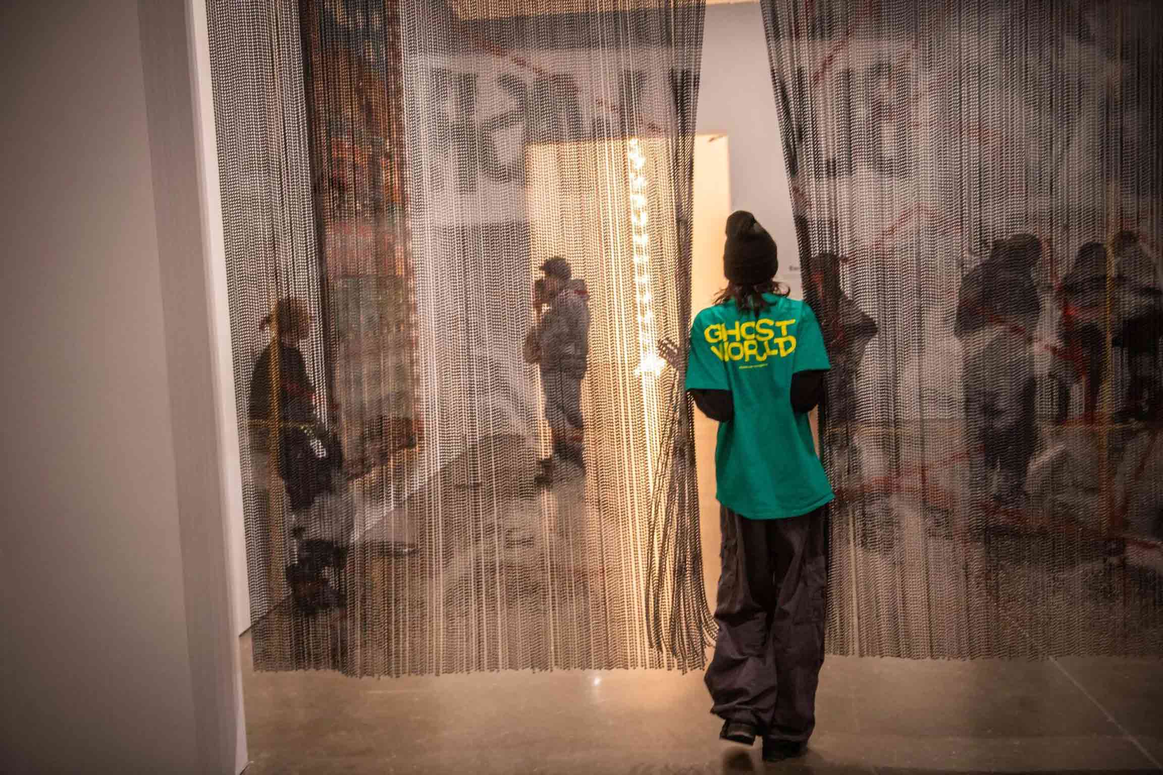 A student, seen from behind parts a metallic mesh curtain to enter a gallery space at the Institute for Contemporary Art, Boston.