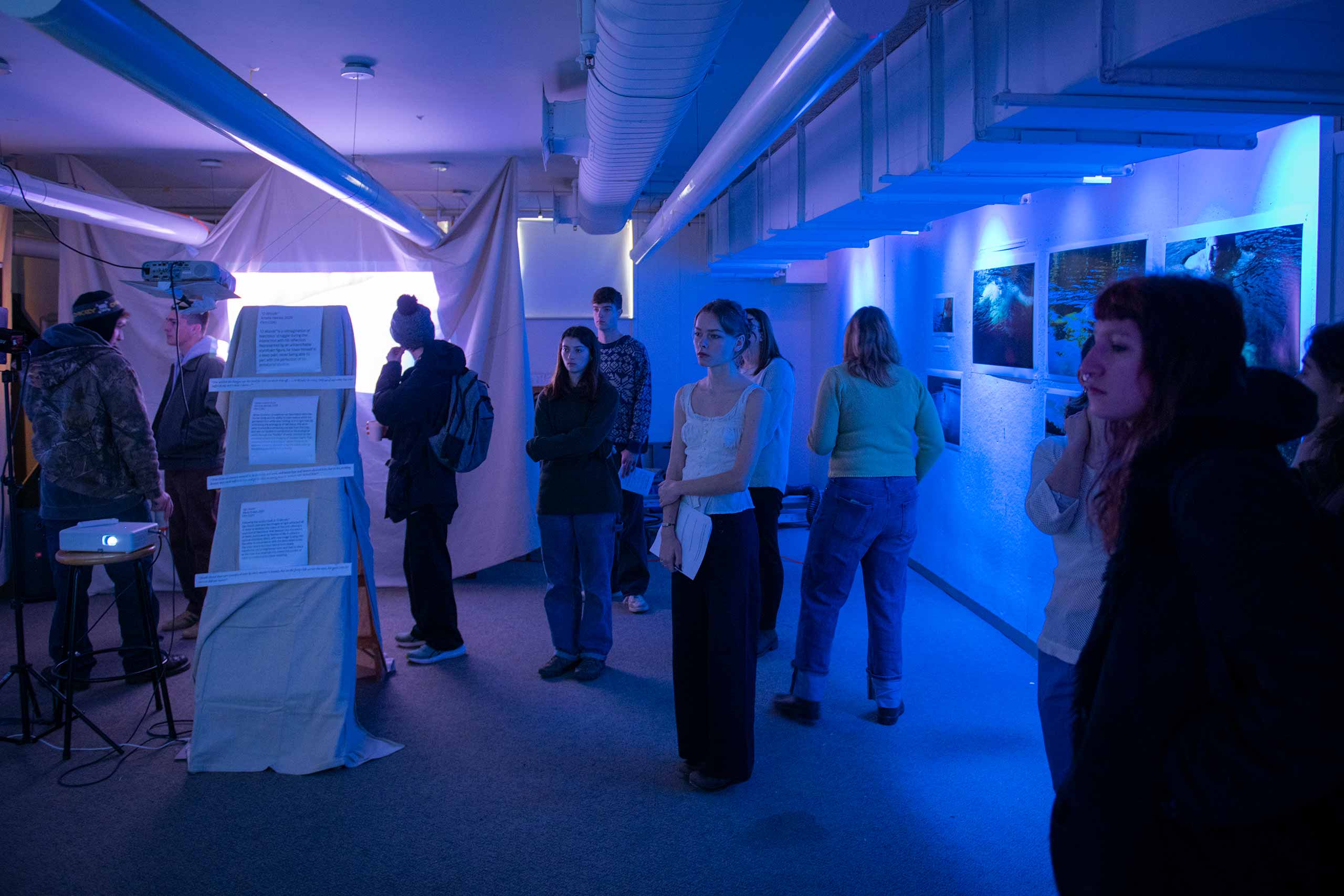 Student view multimedia artworks in dimly lit exhibition space at the Visual and Performing Arts capstone showcase.