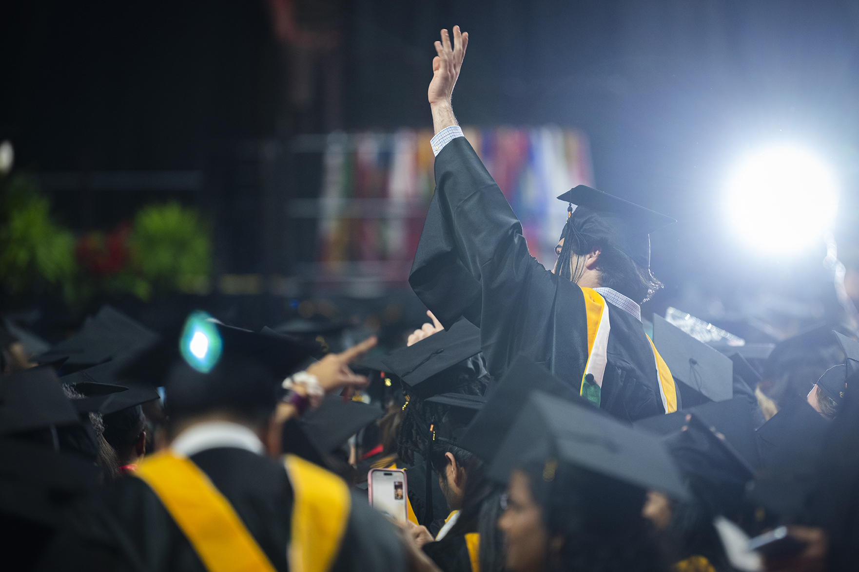 Student in cap and gown waves at Clark University commencement