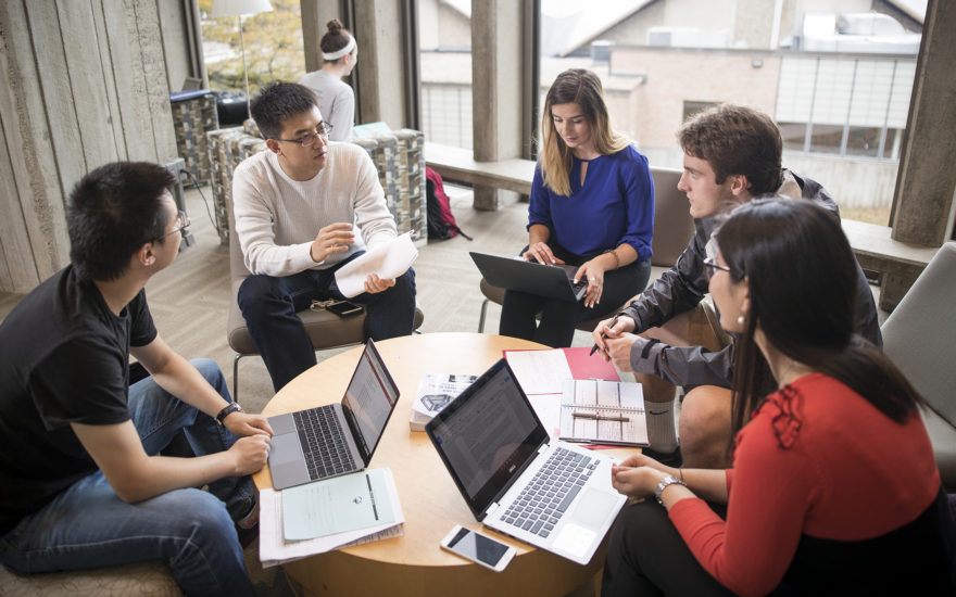 students sitting at table with laptops in a circl