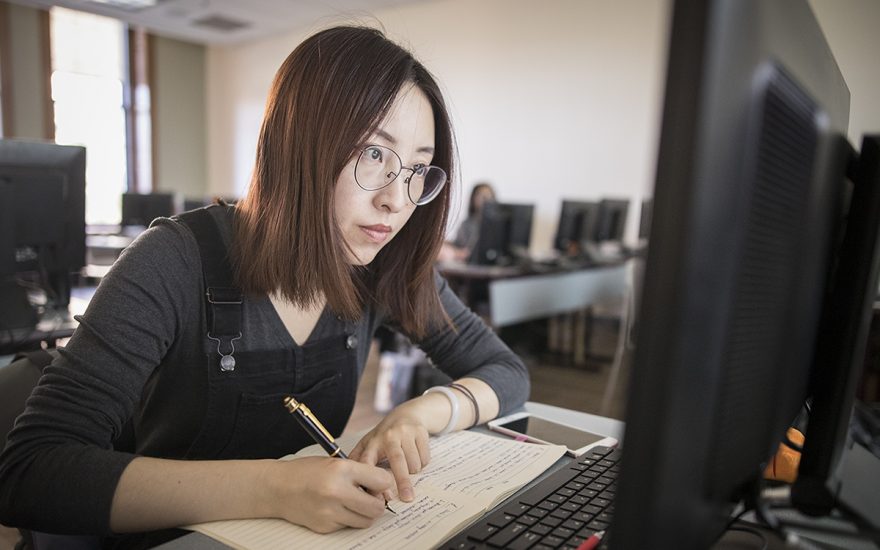 girl writing in notebook and looking at compute