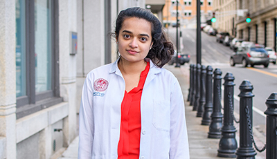 Student standing on street in white coat