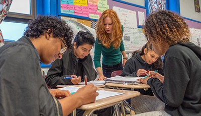 High school students at table with teacher helping