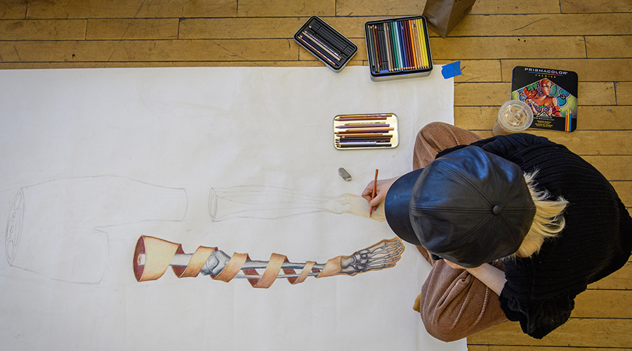 Student painting a self-portrait on sheet on floor in art class