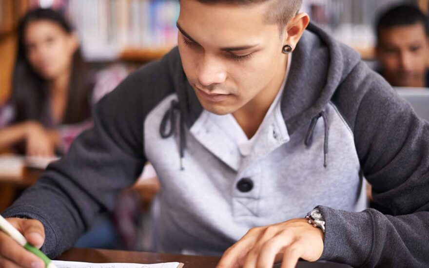 Student writing by hand in a journal in a library setting