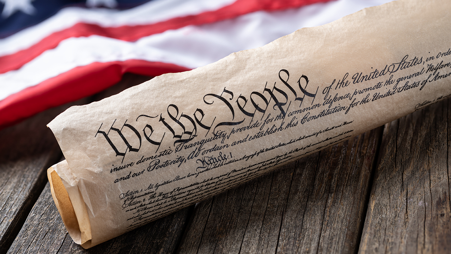 United States constitution with American flag in background on rustic wooden table