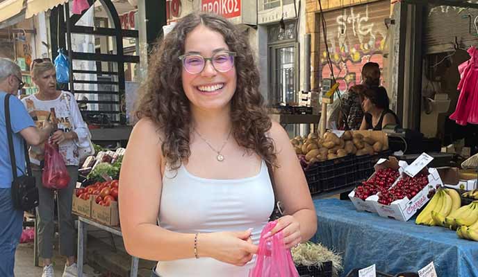 Student holding bag of cherries at a fruit stand during a study abroad trip to Greece