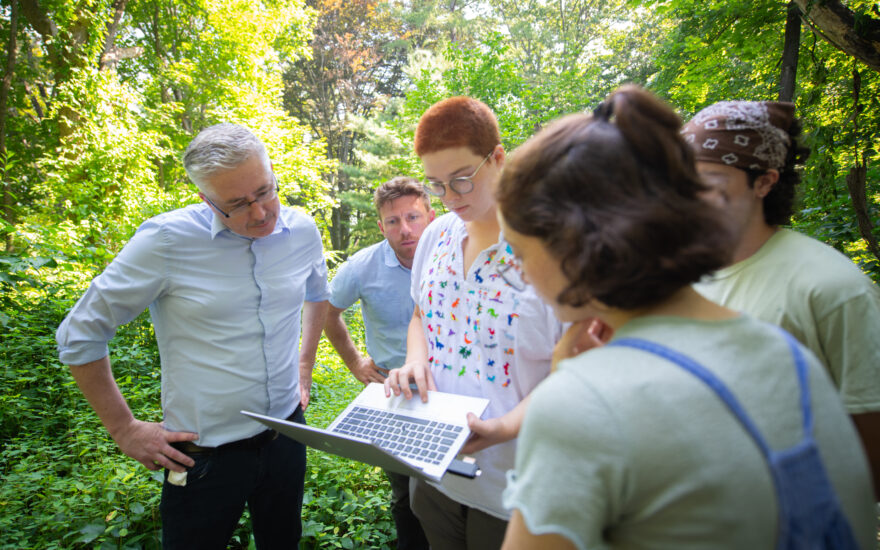 climate and society hero with students looking over laptop in forest