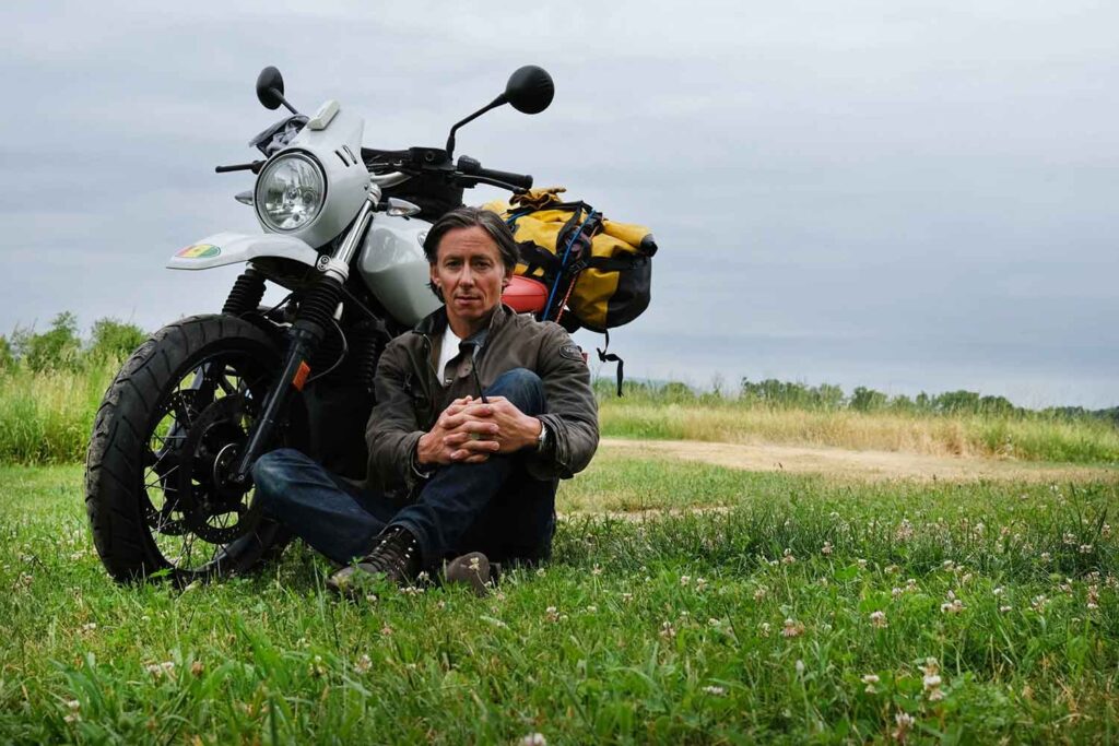 Spencer Platt seated on the grass outdoors beside a motorcycle