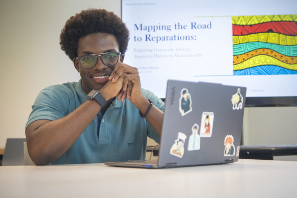 Jonathan Soloman sits in front of a laptop before a Power Point presentation about his reparations GIS project
