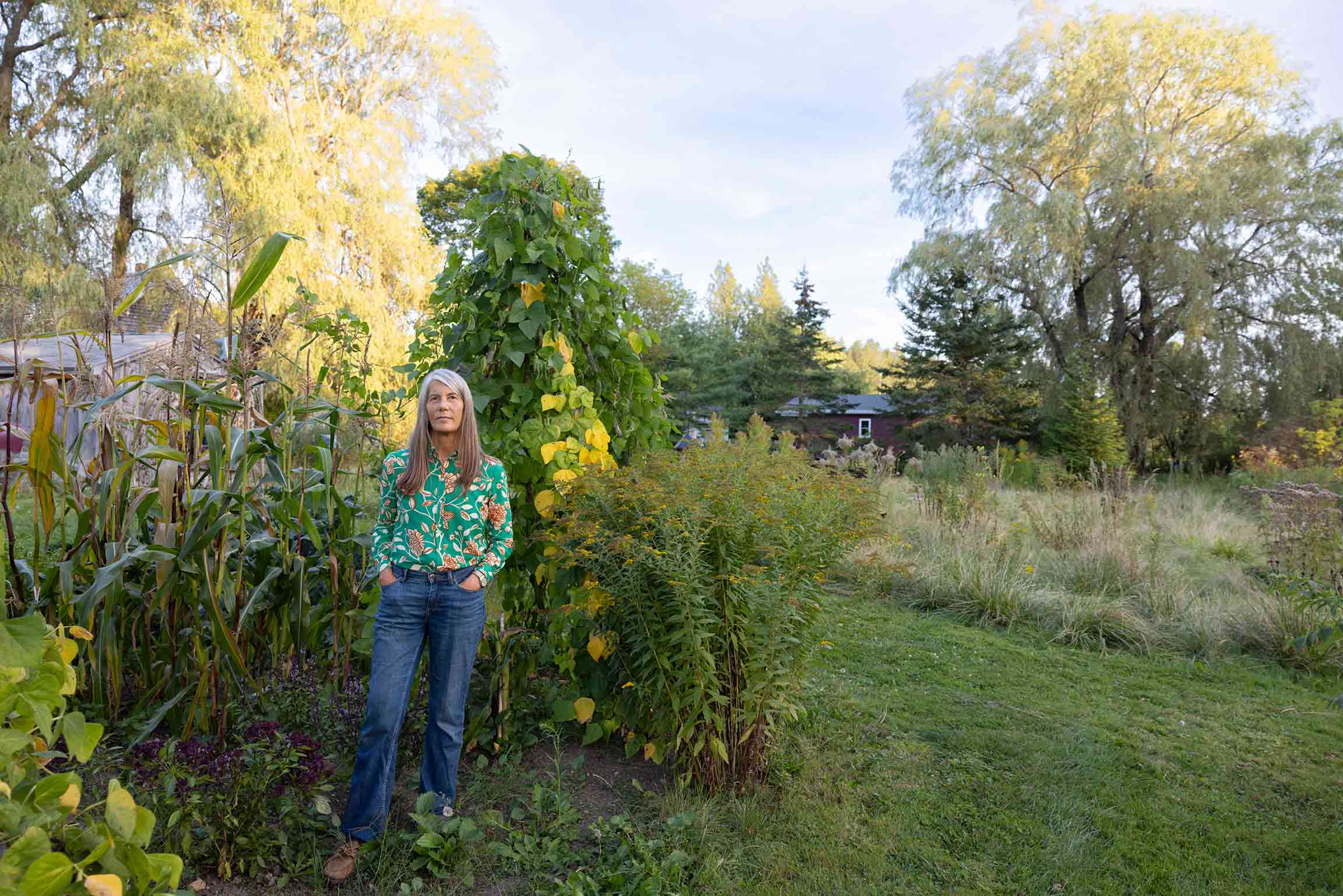 Margaret Wickens Pearce, M.A. ’95, Ph.D. ’98 standing in a garden beside a three sisters companion planting with corn, beans and squash.