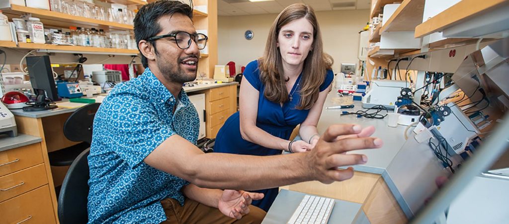 Navid Hossain points to a computer screen while Professor Dresch looks over his shoulder