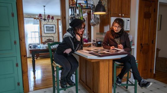 student sitting in kitchen with artist reviewing art