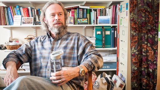 Timothy J. Downs sitting in chair with glass of water