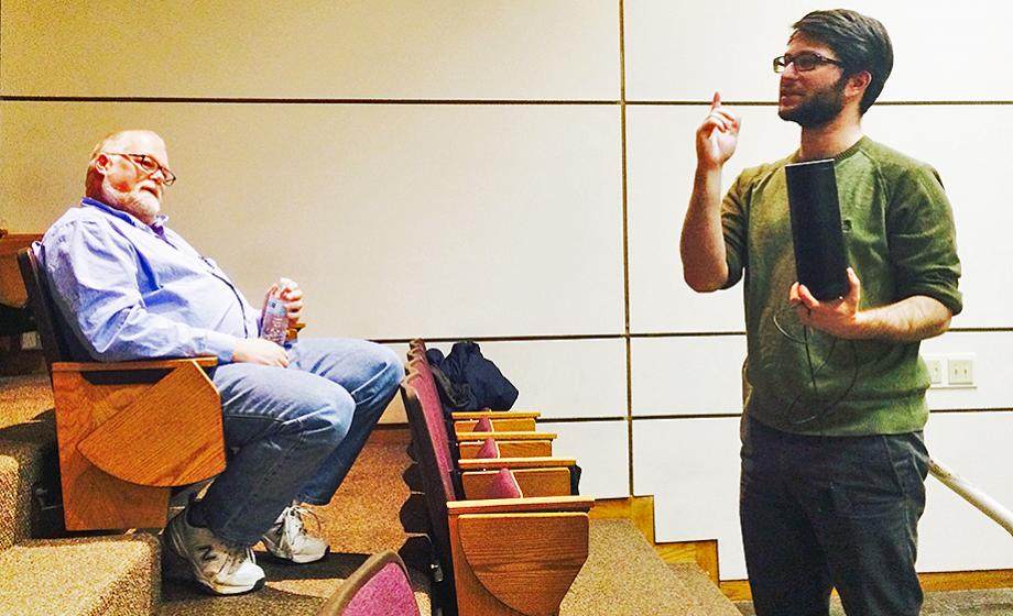 Jake Kramer talks to computer science students while holding an Amazon Echo speaker; visiting professor and former Amazon manager Kenneth Basye watches from the audience