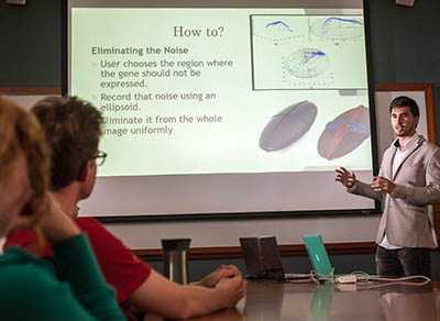 Teodor Nicola-Antoniu ’19, an undergraduate student in Professor Jacqueline Dresch's lab, explains his research to fellow students during Dresch and Robert Drewell's combined biology- mathematics lab meeting.