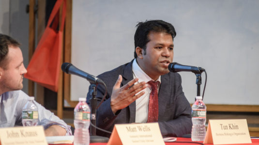 Tun Khin, seated at table, speaks while panelist Matt Wells looks on