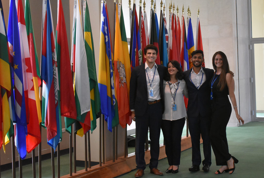 Four students stand in front of flags at United Nations