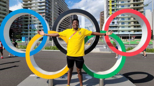 Atuhaire Ambala standing in front of Olympic rings in Tokyo