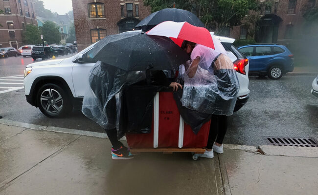 Clark University students huddle under umbrellas while unloading their car during Move-In Day.