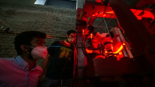 Professor Alexander Petroff uses a large microscope to study bacteria while students look on.