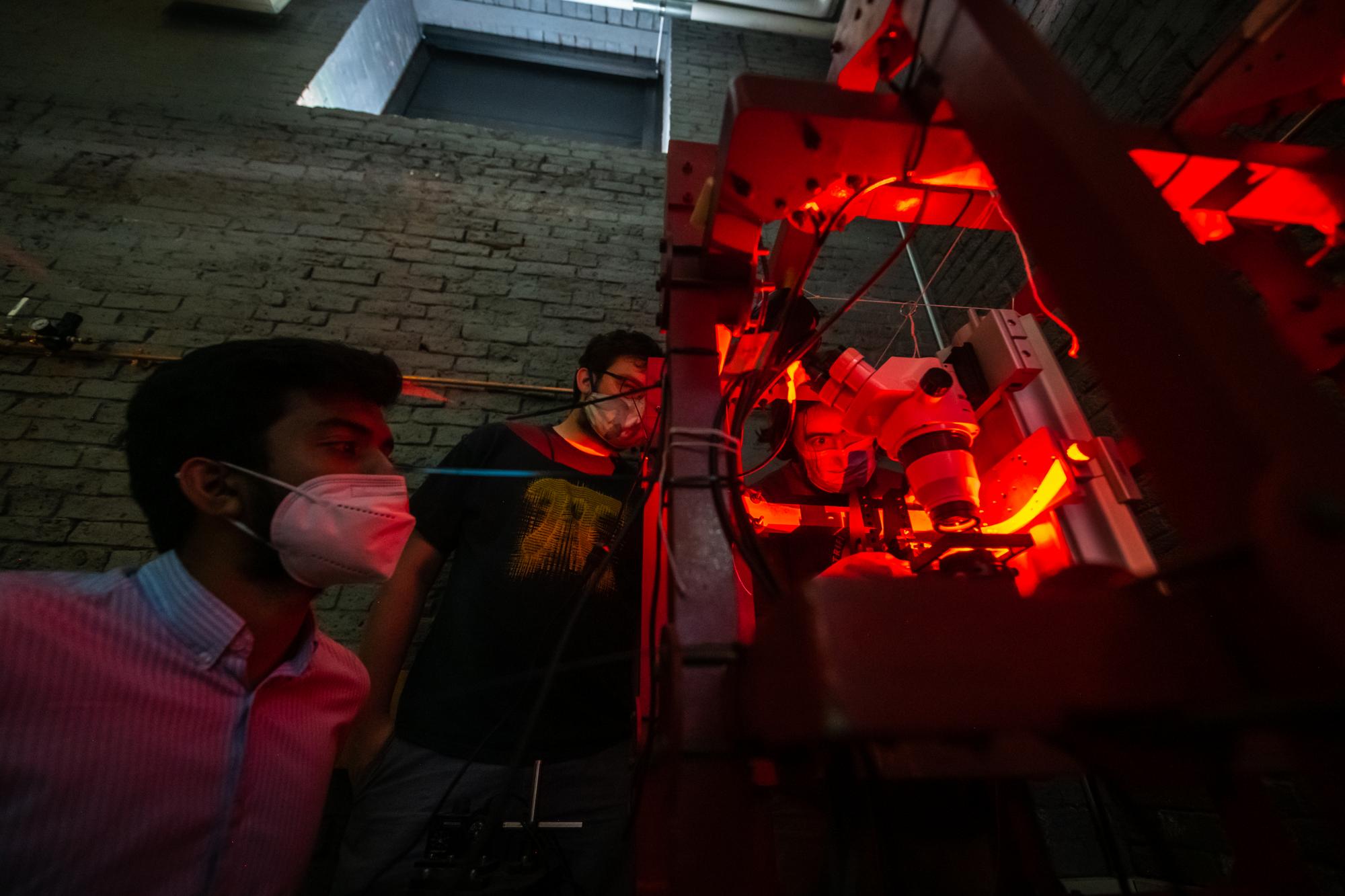 Professor Alexander Petroff uses a large microscope to study bacteria while students look on.